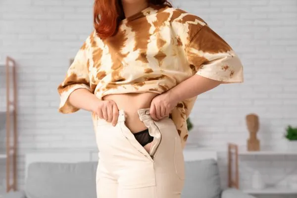 Image of woman trying to do her trousers up after pregnancy weight gain Wantage